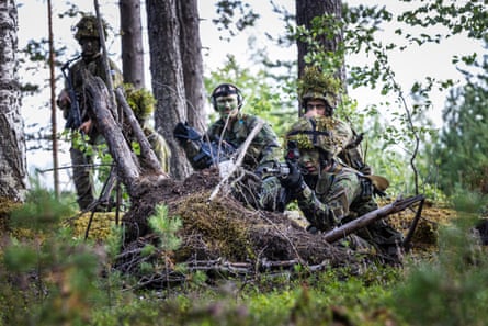 A conscript crouches and aims a gun, watched by colleagues.