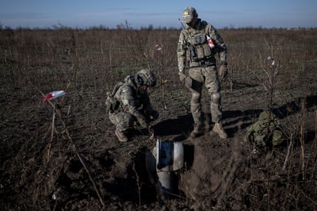 Two men in army fatigues stand in a field next to what looks like a metal shell