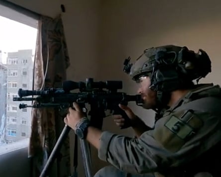 A sniper aims his gun through a window