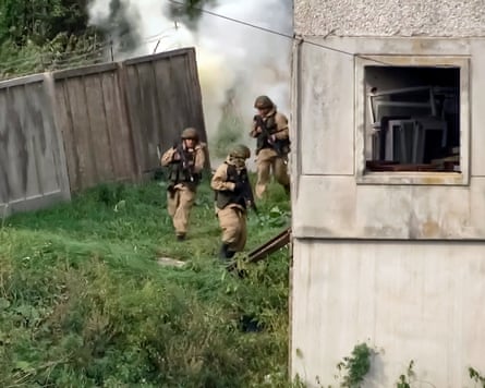 Three soldiers run alongside a derelict building