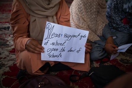 A girl’s hands can be seen holding a handwritten sign reading ‘Please support girls of school. Open the door of schools’