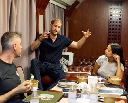 Prince Harry gesturing to fellow passengers in a train dining car