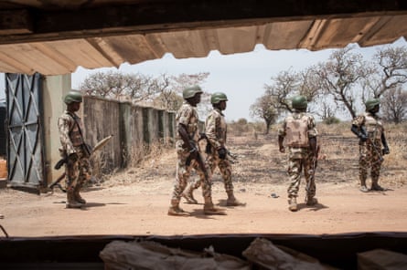 Five soldiers stand outside a concrete structure in a scrubby landscape