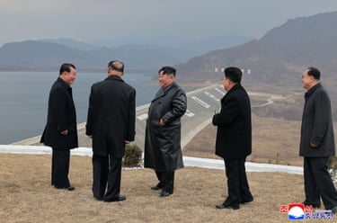 North Korea leader Kim Jong Un, centre, in black with four officials, looks out at a power station from high up which is next to the sea