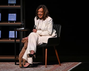 Kamala Harris holds a mic sitting on chair while petting a small dog