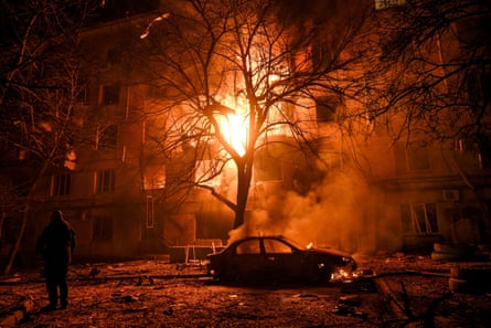 Burnt out car sits in front of a smouldering building