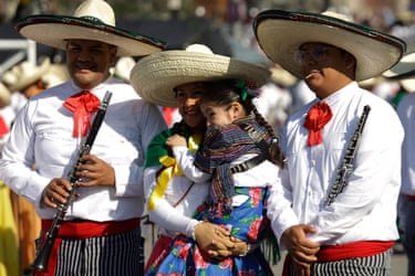 Three people in traditional costume, one holding a child, attend a parade  