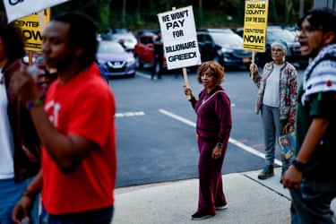 People hold placards reading ‘we won’t pay for billionaire greed!’ on a street