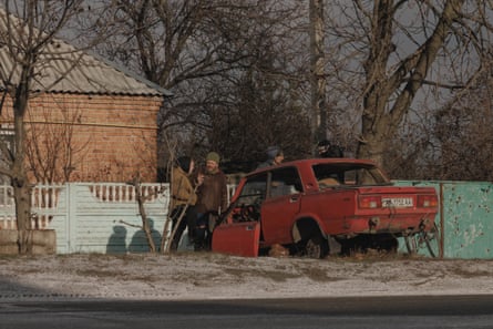 People stand next to a damaged car outside a house 