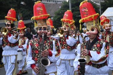 People in colourful costumes, masks and hats play instruments