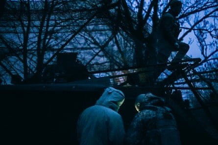 In the light of early morning dusk, the driver sits on top of the vehicle. Below, two soldiers with their backs to the camera check the route for the rotation