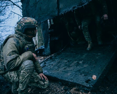 A soldier crouches down and looks into the armoured carrier as soldiers walk out