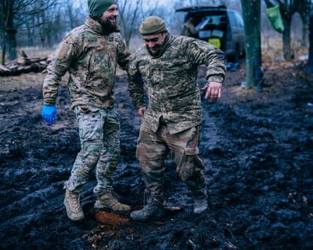 A man limps across the mud helped by a fellow soldier