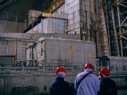 Three people in red hard hats inside the grey concrete safe confinement shelter