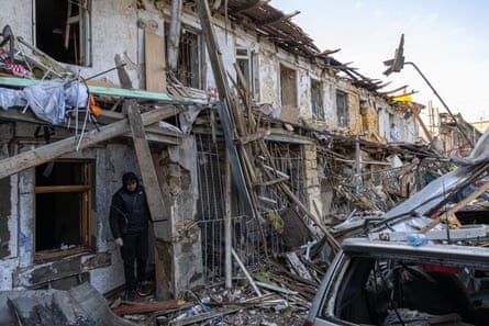 A man stands amid debris and damage from a small terrace of houses hit by munitions