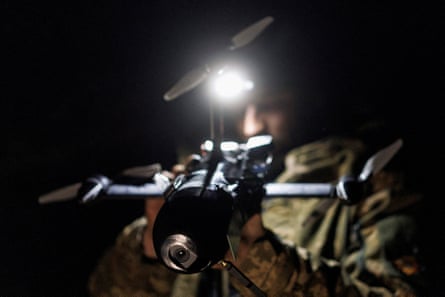 A man in military fatigues and wearing a head-torch prepares a drone at night