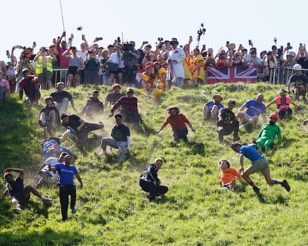 People scrambling down a hill on a sunny day during a cheese-rolling competition