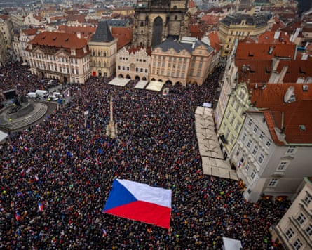 An aerial shot of a large crowd of people in Prague’s Old Town Square carrying a huge Czech flag between them.