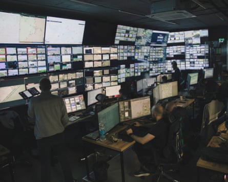 People sitting at computers with banks of screens on the wall in front of them