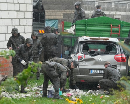 Members of the military clean up debris from the destroyed roof of a house, next to a dented car