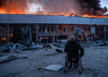 A man in a wheelchair looks at a burning building with his back to the camera