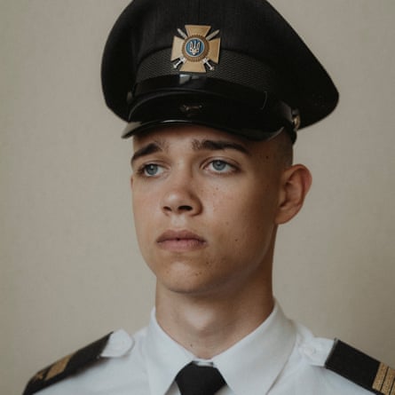 Head and shoulders portrait of seventeen-year-old Zakhar Yanov: he has blue eyes and thick, dark eyebrows, and wears a tall cap with a metal cross-shaped badge and a white shirt with black epaulettes and a black tie. He looks serious and resolute.