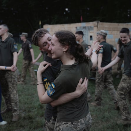 Male and female cadets dancing outdoors on the grass: they are casually dressed in short-sleeved khaki shirts with badges on the sleeves and camouflage combat trousers.