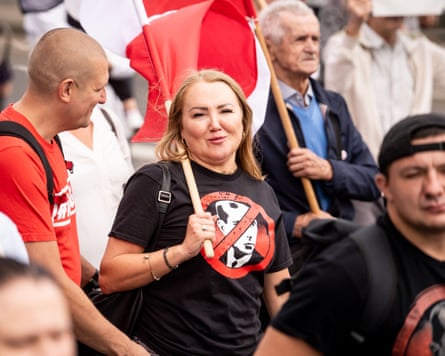 A woman and a man in a crowd both wear black T-shirts showing the face of Stepan Bandera within a crossed out red ring