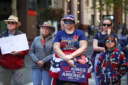 a person holds a sign that reads ‘no kings in America since 1776’ while wearing a shirt that reads ‘radicalized by basic decency’