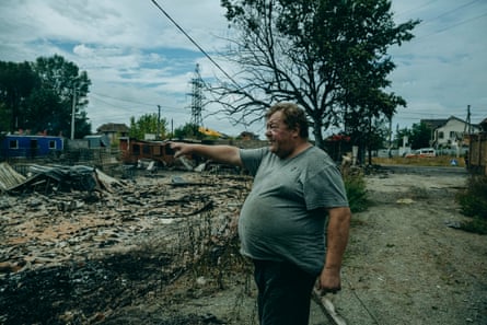 A heavy-set man points across a burnt-out field 
