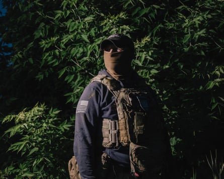 Panama stands against tree foliage in a blue military jacket, his face obscured by a cap and neck gaiter
