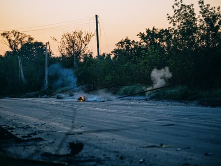 A drone in flames and smoke lies on a road.