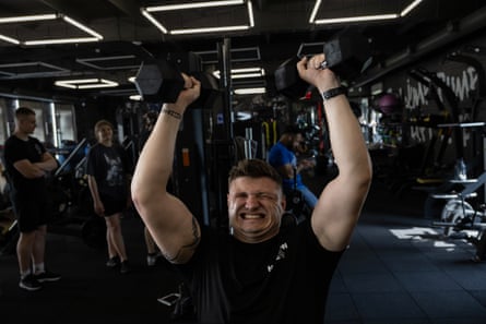 Vitaliy Veres lifts dumbbells above his head in a dark gym 
