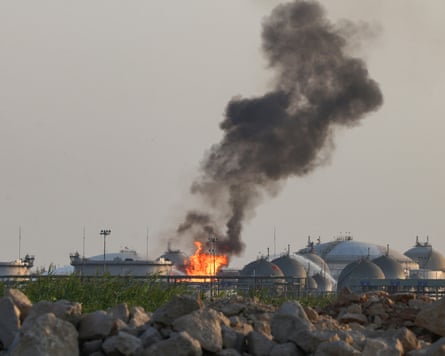 Flames and thick black smoke rise from Aramco’s Riyadh refinery, viewed over a rocky field