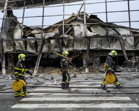 Rescuers carrying hose reels walk past a missile-damaged shopping centre in Kyiv