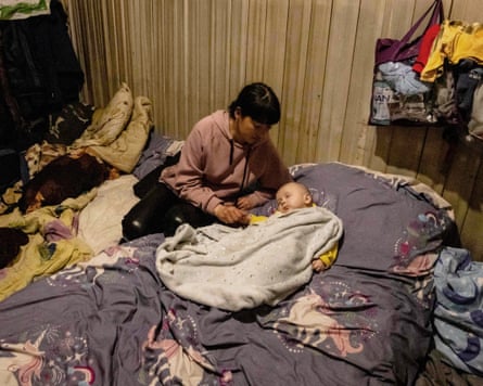 A woman takes care of a baby in a shelter with mattresses and bedding strewn around.