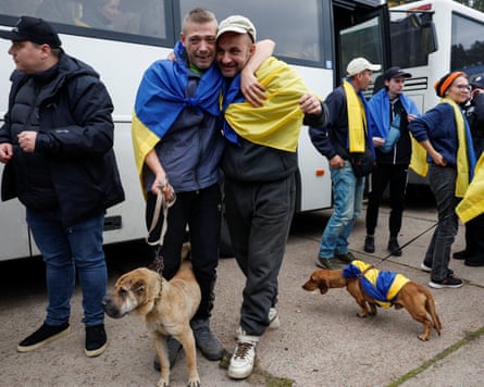 Evacuated residents embrace tearfully in Ukrainian flags, with dogs beside them near a bus