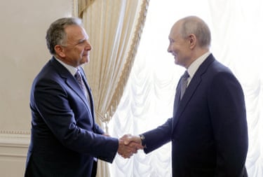 Vladimir Putin shakes hands with Steve Witkoff, both smiling near a curtained window