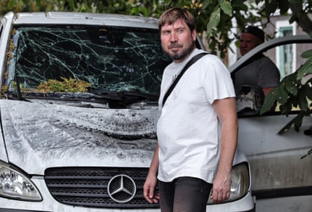 A man walks past a white Mercedes car with its windscreen shattered and bonnet dented and blackened. 