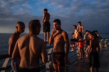 Teenagers gather on a Batumi pier railing by the sea at dusk, waiting to jump into the water