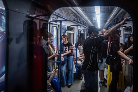 Passengers stand closely packed, holding rails and phones inside a crowded Tbilisi subway carriage