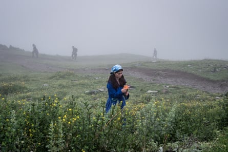 A woman picks flowers in a misty hillside meadow near Gergeti Trinity church