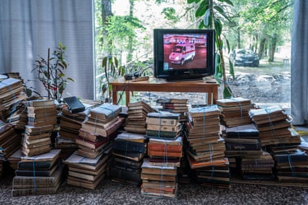 Stacks of bundled old books fill a museum room, with a television playing beside a window