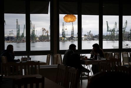 Customers dining in a restaurant with a harbour beyond.