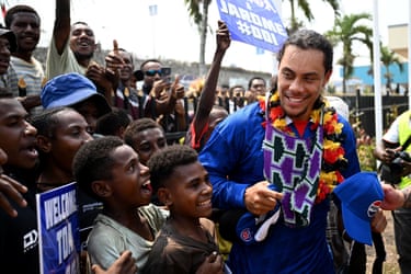 Jarome Luai, wearing a flower garland, smiles while greeting excited young fans outside an airport